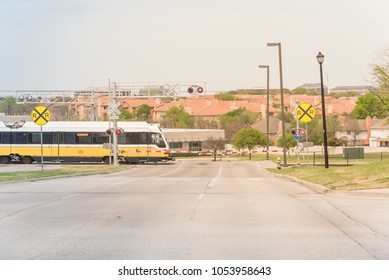 Light Rail Train Speeding Through A Red Alert Sign Level Crossing In Downtown Las Colinas, Irving, Texas, USA. Railway Line Intersection With Barrier Gate Closing