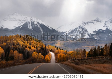 Light rays shine down on a scenic road in Colorado surrounded by mountains and fall colors. An autumn mountain scene near Mountain Village & Telluride, CO. 