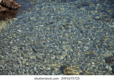 Light refracts through deceptively deep, crystal-clear water in Mali Losinj, Croatia.Pebbles stones in transparent water.Clear water reveals an array of smooth pebble stones beneath the surface.