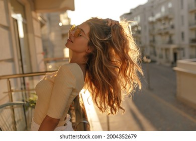  helles, entspannendes Bild von Mädchen in Brillen, Nahaufnahme unter Sonneneinstrahlung. Steht auf dem Balkon und streckt ihr langes Haar nach Seiten aus. Sie sonnenbadet gerne.