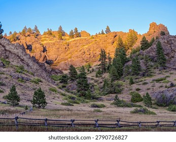 The light of the setting sun is illuminating the cliffs above a buck rail fence near Craig, Montana, USA