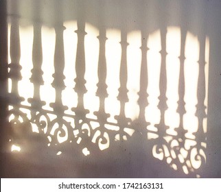 Light and shadow on the white wall from wrought iron gate in the morning with yellow bright tone.