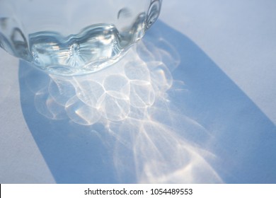 Light And Shadow From Sunlight Reflect To Water Glass On White Background.