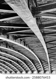 Light and shadows emphasize the structure of the beams and girders of a bridge crossing the Seine River in Paris. In black and white.