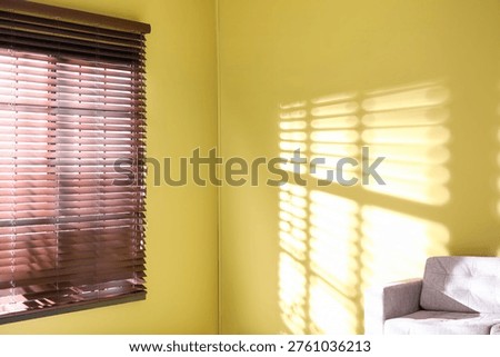 Light and shadows from window blinds falling on green wall