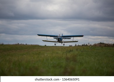light single-engine private plane biplane takes off from the airport very close, gaining altitude for the flight with passengers in the air, blue and white hull against the cloudy sky and green grass