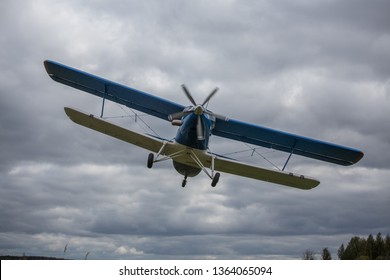 light single-engine private plane biplane takes off from the airport very close, gaining altitude for the flight with passengers in the air, blue and white hull against the cloudy sky and green grass