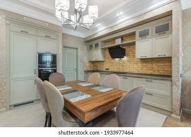 The light and spacious kitchen with built-in appliances. The square dining table with soft chairs standing in the center of the kitchen