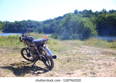light sports bike is parked on the sandy shore of the lake on a summer day, green landscape, recreation and unity with nature after a long trip on two-wheeled transport
