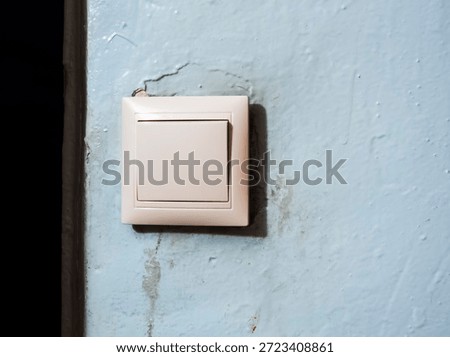 Light switch mounted on cracked, peeling blue wall showing wear, decay and exposed wiring symbolizing household electricity, repair, maintenance and aging infrastructure