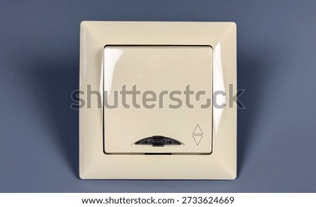 A light switch is mounted on a gray wall in a house. It has a simple design. The switch is commonly used to control the lighting in the room.