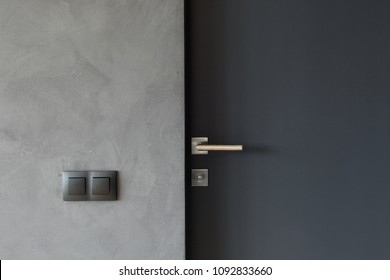Light switch on the gray textured wall next to the door with metallic handle - Shutterstock ID 1092833660