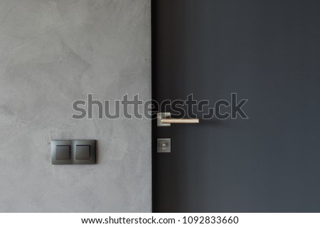 Light switch on the gray textured wall next to the door with metallic handle