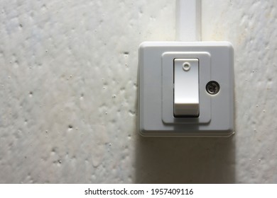 Light switch with sunlight and shadow on white wall with texture in the dark. Button in dim light.