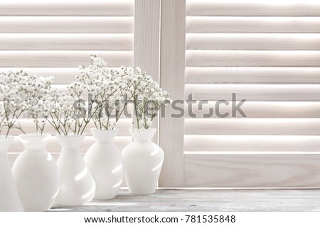Light through the wooden shutters and blinds.Small white flowers on a white background. Soft home decor. Gypsophila flowers. White flowers in a vase. Retro style.