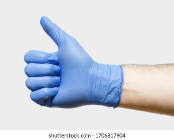 Light Thumb up male hands in blue medical gloves over light gray background. Closeup