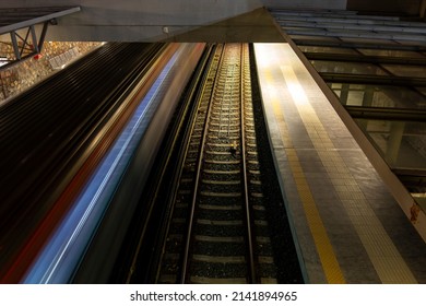 Light trail of quickly driving metro train at night in Athens, Greece with a platform and second railroad