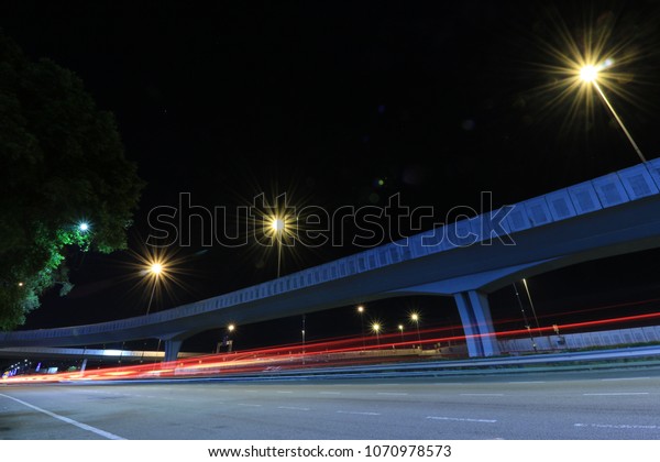 Light trails of cars passing by the Lebuhraya Sultan\
Iskandar at night. Background of an elevated interchange, lamps and\
night sky.
