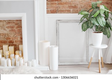 Light White Interior Photographed With Natural Light. Flat Brick Wall With Fake Fireplace, Candles, Roll Of Papers And House Plant On The Table