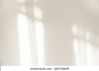 The light from the window shines on the white wall, the shadow from the curtain, blurry shadows and silhouettes on the wall.