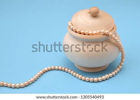 Light wooden sugar bowl with a lid and a string of sea pink pearls on a blue background. Wooden unpainted barrel preparation for creativity