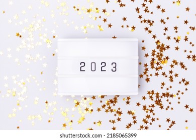 Lightbox With 2023 Numbers On A Blue Pastel Background With Golden Stars Confetti.