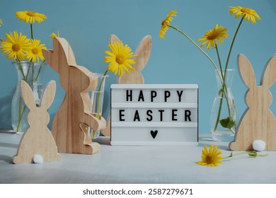 Lightbox with message HAPPY EASTER on festive blue background and eco-friendly zero waste natural decoration. Yellow daisies flowers. Holiday