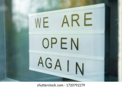 Lightbox with as sign we are open again behind a glass door of the cafe. We're open again after quarantine, video of small business owner. Please wear a face mask and keep your distance to protect