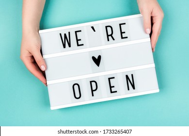 Lightbox with the text We're Open on a blue background in women's hands. - Shutterstock ID 1733265407