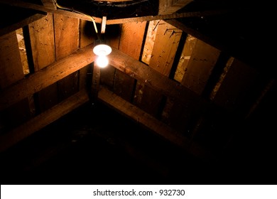 A lightbulb in the ceiling of an attic with nails sticking through the roof and cobwebs