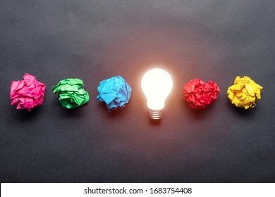 Lightbulb and crumpled colorful paper balls on black background. Successful solution of problem. Idea generation and brainstorming. Genius idea among failing ideas metaphor. Business motivation