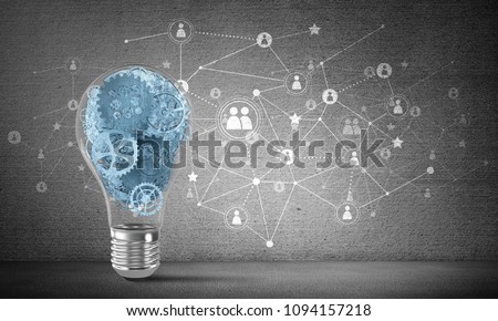 Lightbulb with multiple gears inside placed against social network system on grey wall. 3D rendering.