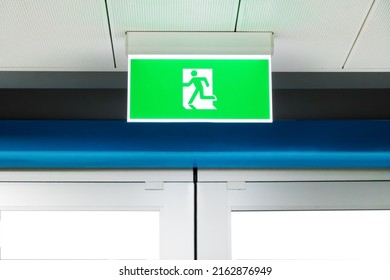 Lighted glowing green emergency exit signs in an office hallway with pointing the way out of the building.