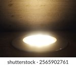 A lighted hole in a wall. The light is shining on the wall and the hole. The light is bright and the hole is round