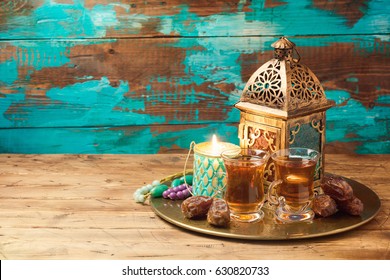 Lightened lantern, tea cups and dates on wooden table over rustic background. Ramadan kareem holiday celebration concept