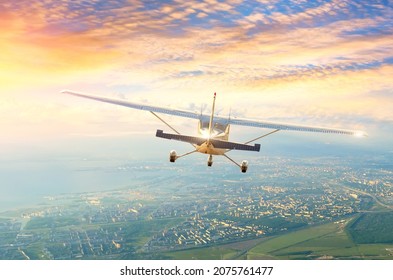 Light-engine plane flies in the morning sky clouds at dawn over the city, back view