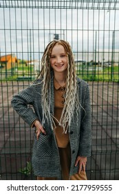 Lighthearted teenage girl with dreads standing in front of a metal fence. She is wearing a jacket. Portrait. - Shutterstock ID 2177959555