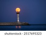 Lighthouse beacon and full moon twilight over sea horizon and moonlight in ripple water