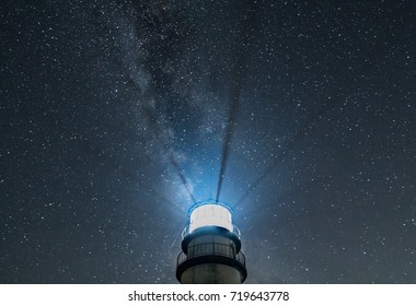 Lighthouse beacon rays shining against starry sky and Milky Way