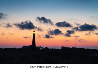 Lighthouse in the dunes and clouds during sunset.
