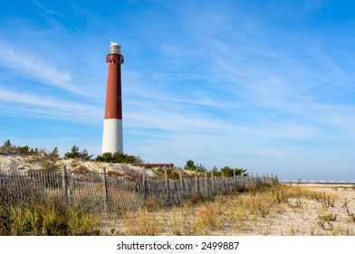 A lighthouse on the beach. There is also an old wooden fence on the beach in this landscape. This is Barnegat Lighthouse, nicknamed "Old Barney", at Long Beach Island, New Jersey.