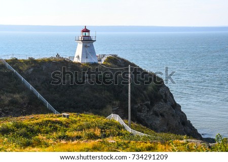 The lighthouse on Cape Enrage, New Brunswick, Canada, on the edge of the rocky angled cliff with fencing and poles at angles