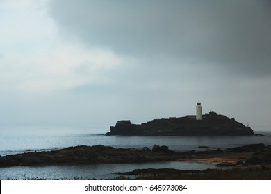 A lighthouse on a dark rocky island, dark skies above. Cornwall, UK.