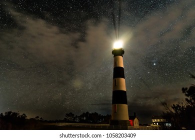 Lighthouse On The Outer Banks Shining Brightly In The Night In Front Of Clouds And A Huge Sky Full Of Stars And The Milky Way