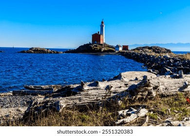 A lighthouse is on a rocky island in the ocean. The water is calm and the sky is clear - Powered by Shutterstock