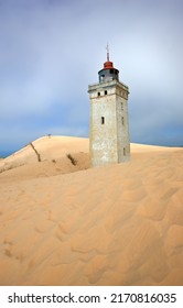 Lighthouse on a sand dune by the sea against a blue sky. Mysterious old tower alone in the desert. Deserted lighthouse isolated on beige sand. Peaceful and tranquil nature scene in Jutland, Denmark.