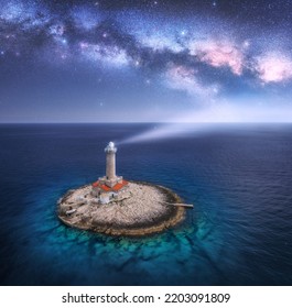 Lighthouse On Smal Island In The Sea And Milky Way At Night In Summer. Aerial View Of Beautiful Lighthouse With Light Beam On The Rock, Purple Sky With Stars. Landscape. Adriatic Sea, Croatia. Space