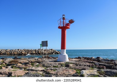 Lighthouse On Wave Breaker And Stone Pier At Sea. View Of The Mediterranean Sea With The Lighthouses At Rocky Shore. Wave Breakers Along The Shoreline With Lighthouse At Ocean. Lighthouse On Blue Sky.