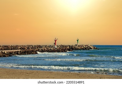 Lighthouse On Wave Breaker And Stone Pier At Sea. View Of The Mediterranean Sea With The Lighthouses At Rocky Shore. Wave Breakers Along The Shoreline With Lighthouse At Ocean. Lighthouse On Sunset.