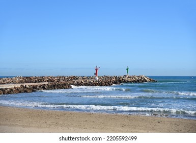 Lighthouse On Wave Breaker And Stone Pier At Sea. View Of The Mediterranean Sea With The Lighthouses At Rocky Shore. Wave Breakers Along The Shoreline With Lighthouse At Ocean. Lighthouse On Blue Sky.